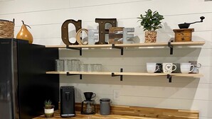 Una cocina moderna con armarios blancos, encimera de madera y microondas integrado. Hay repisas con varios utensilios de cocina y un letrero decorativo.