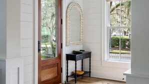 A hallway with a wooden door, a mirror, a small table, and a window with a view of greenery.