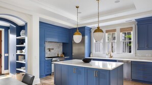 A modern kitchen with blue cabinetry, a large island, and pendant lighting.