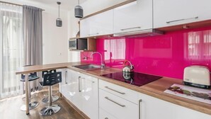 Eine moderne Küche mit weißen Schränken, einer rosafarbenen Spritzschutzleiste und einer Holz Arbeitsplatte. Auf der Arbeitsplatte steht ein Wasserkocher und ein Toaster.