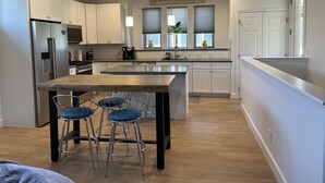 A modern kitchen with white cabinets, a stainless steel refrigerator, a wooden island with bar stools, and a pendant light. - Family friendly Grover Beach house located blocks from the ocean.    (Grover Beach)
