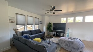 A modern living room with a grey sofa, a bean bag, a TV, and a ceiling fan. - Family friendly Grover Beach house located blocks from the ocean.    (Grover Beach)