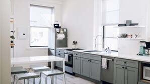 Une cuisine moderne avec des meubles gris, un plan de travail blanc et un four encastré. On y trouve des tabourets de bar et une fenêtre qui laisse entrer la lumière naturelle.