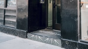 L’extérieur de l’hôtel The Neighborhood se distingue par sa façade noire, ses grandes fenêtres et sa porte d’entrée bien visible.