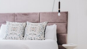 Une chambre à coucher avec un lit blanc, une tête de lit rose, une petite table de chevet blanche et un tapis à carreaux.