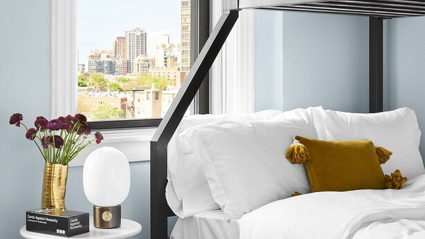 A modern bedroom with a bunk bed, a small side table with a vase and a card, and a patterned rug.