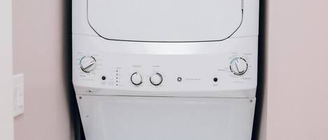 A white washing machine installed in a bathroom with a pink wall.