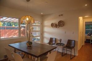 Un coin repas avec une table en bois, des chaises, un luminaire suspendu et une vue par la fenêtre.