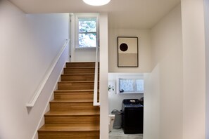 A staircase with wooden steps and white handrails leading to a room with a washing machine and a window.