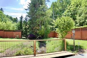 A wooden deck with a metal fence, surrounded by a garden with various plants and trees.