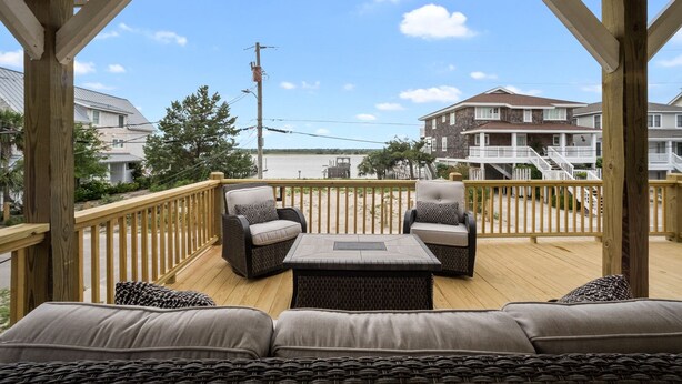 A covered deck with wicker furniture and a view of the beach and houses.