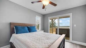A bedroom with a bed, a ceiling fan, and a view of the outdoors through a sliding door.