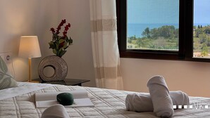 A bed with a view of the sea, a lamp, a vase with flowers, and a small table with a decorative item. - Villa EL HORIZONTE in Benissa – For 4 people with sea views, swimming pool and barbecue (Benissa)