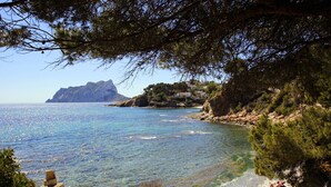 A coastal landscape with clear blue sea, rocky shore, and a mountain in the distance. - Villa EL HORIZONTE in Benissa – For 4 people with sea views, swimming pool and barbecue (Benissa)