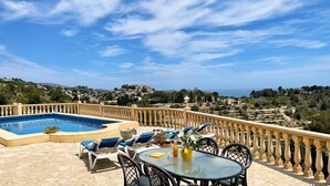 A rooftop pool area with lounge chairs and a table, overlooking a scenic landscape with a view of the sea and distant hills. - Villa EL HORIZONTE in Benissa – For 4 people with sea views, swimming pool and barbecue (Benissa)