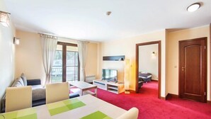 Hotellihuone, jossa on ruokailutila, televisio, sänky ja punainen matto.
