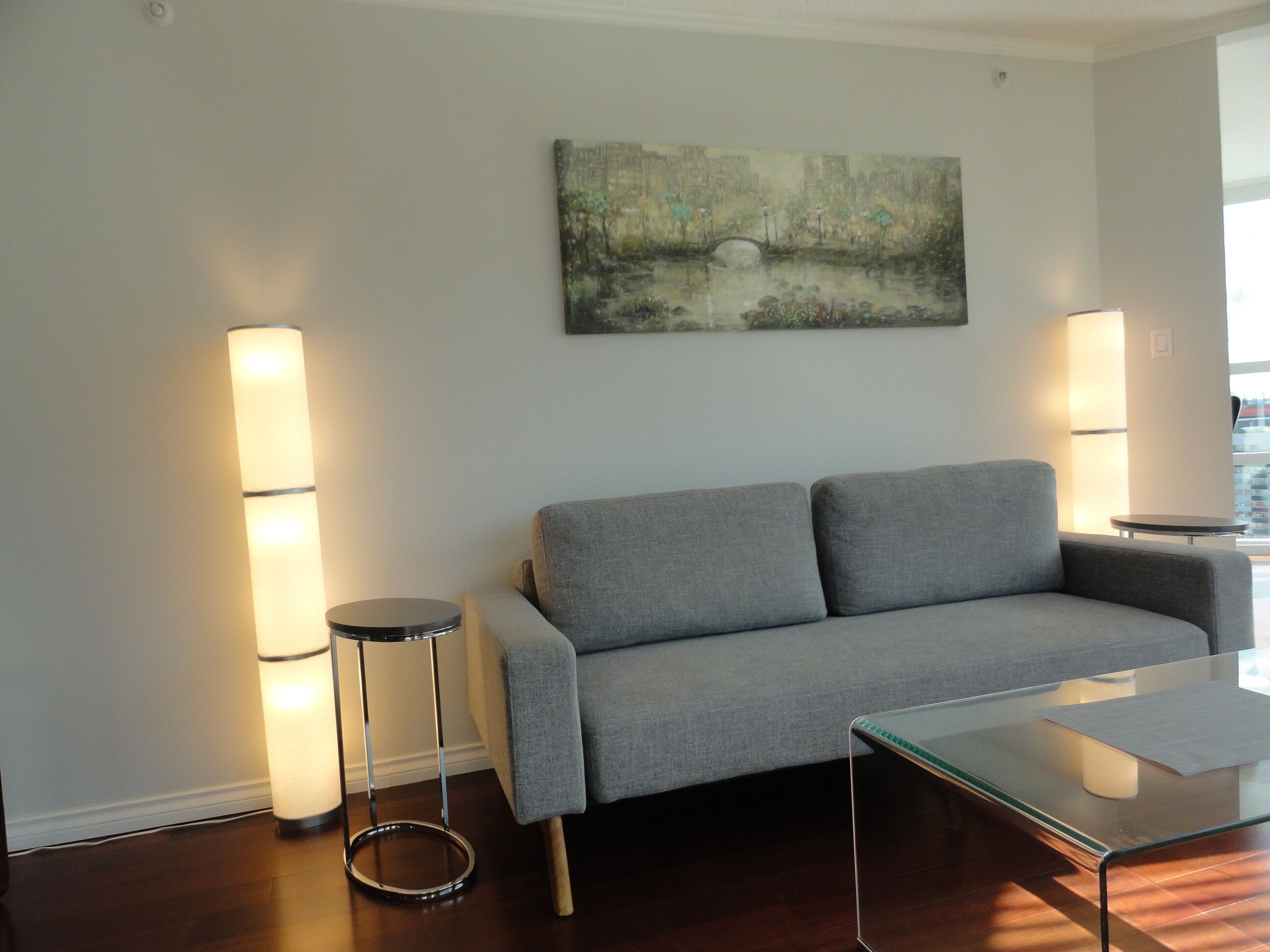 A modern living room with a grey sofa, a glass coffee table, and two tall floor lamps.