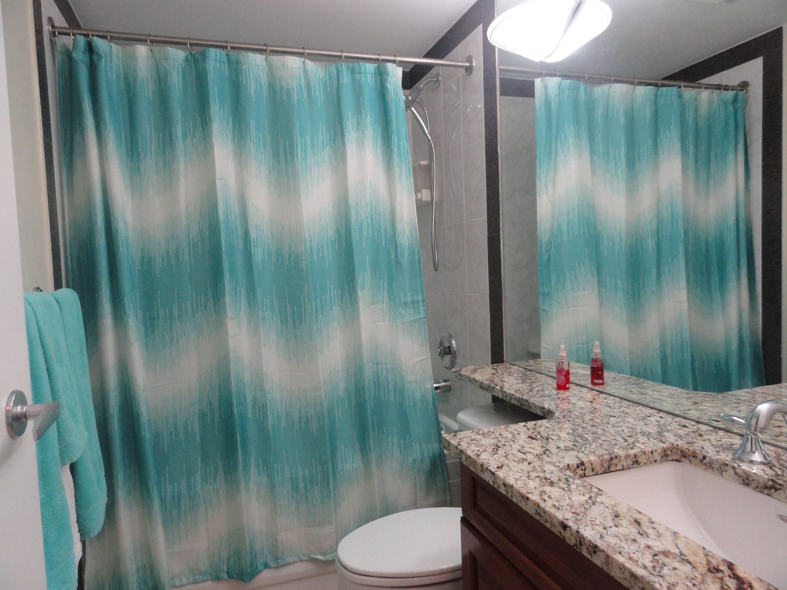 Un baño con cortina de ducha, inodoro, lavamanos con espejo y un perchero para toallas.