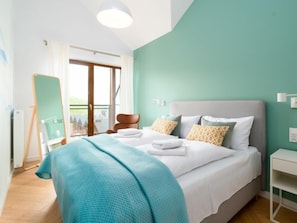 A bedroom with a bed, a bedside table, a chair, a window, and a view of buildings outside.