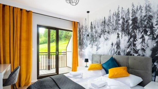 A modern hotel room with a large bed, a desk, and a balcony with a view of greenery.