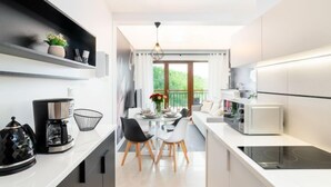 A modern kitchen with white countertops, a coffee maker, and a dining area with a table and chairs.