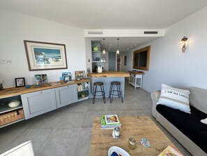 Uma cozinha moderna com uma ilha central, banquetas de bar, um espaço de refeições com um sofá e um quadro na parede.