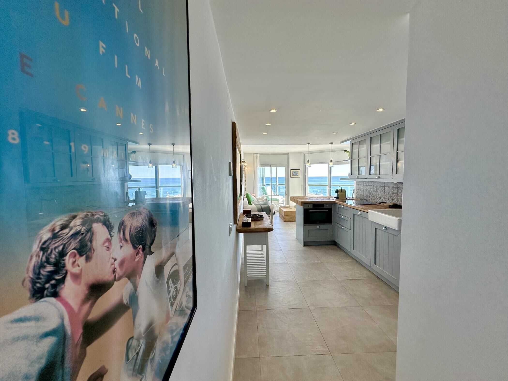 A modern kitchen with grey cabinets, a wooden countertop, and a view of the sea.