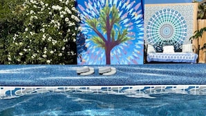 A swimming pool with clear blue water, a tree mural, and a circular tapestry. - Relax Close to Park, Hot Tub, Hammocks, Private, Lush Trees (Joshua Tree)
