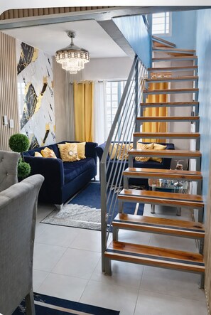 A modern living room with a blue sofa, a chandelier, and a wooden staircase.