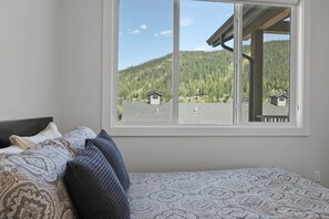 Un dormitorio con un ventanal que ofrece vistas a una montaña boscosa y pequeñas cabañas.