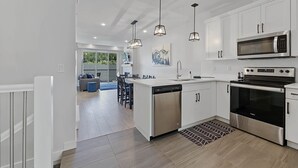 A modern kitchen with white cabinets, stainless steel appliances, and pendant lighting. - Townhome with Garage, 3 Bedrooms and Hot Tub (Sun Peaks)
