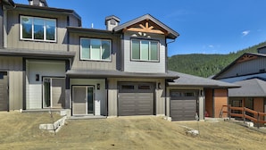A two-story house with a garage and a covered porch. - Townhome with Garage, 3 Bedrooms and Hot Tub (Sun Peaks)