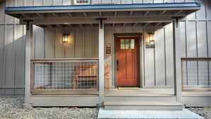 Ein hölzernes Gebäude mit roter Tür, einer Bank und zwei Wandleuchten.