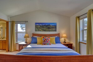 A bedroom with a wooden bed, two bedside tables with lamps, a window with curtains, and a mountain landscape painting on the wall. - Pet Friendly!  Fireplace, Fenced Yard, Mountain Views, Near Hot Springs (Pagosa Springs)