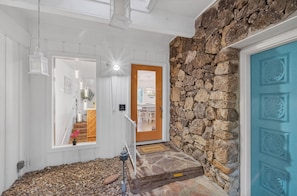 A staircase leading to a room with a stone wall and a blue door, a white railing, and a welcome mat.