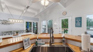 Une cuisine moderne dotée d’un évier en acier inoxydable, de plans de travail en bois, d’un ventilateur de plafond et offrant une vue sur l’extérieur.