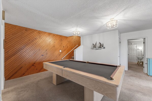 Ein Billardtisch in einem Raum mit schrägverdeckter Holzdecke und einer weißen Wand mit einer Segelboot-Dekoration.