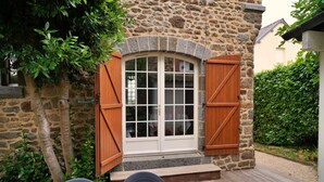 Ein Steinhaus mit Holztür, einem Fenster und einer kleinen Außenbereich-Sitzgelegenheit mit Stühlen und Tisch.