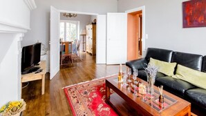 Ein Wohnzimmer mit einem schwarzen Ledersofa, einem Couchtisch mit Weingläsern und einer Flasche sowie einem roten Teppich mit Muster.