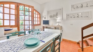 A dining area with a table set for two, a television, and artwork on the walls. - Casa Le Palme with an equipped outdoor area (Porto Azzurro)