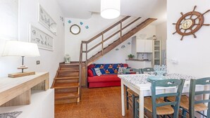 A cozy interior with a wooden staircase, a red sofa, a dining table with chairs, and a wall clock. - Casa Le Palme with an equipped outdoor area (Porto Azzurro)