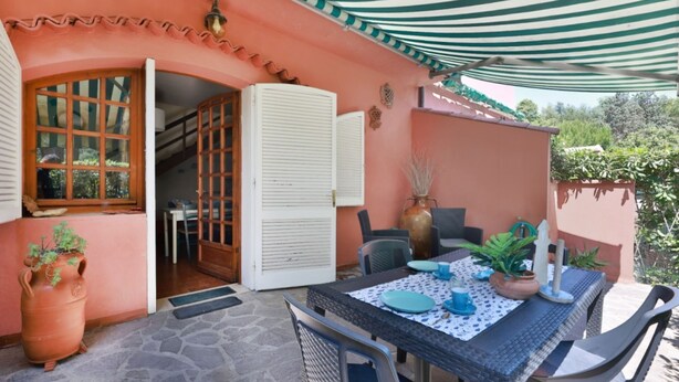An outdoor patio with a table set for dining, a potted plant, and a door leading to an interior space. - Casa Le Palme with an equipped outdoor area (Porto Azzurro)