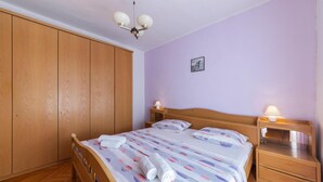 A bedroom with a wooden wardrobe, a bed with a patterned bedspread, two bedside tables with lamps, and a ceiling fan. - Nice Apartment in Valtura With 2 Bedrooms (Liznjan)