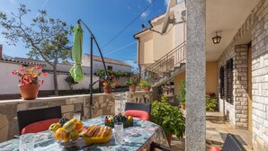 An outdoor seating area with a table set for two, surrounded by potted plants and a staircase leading to an upper level. - Nice Apartment in Valtura With 2 Bedrooms (Liznjan)