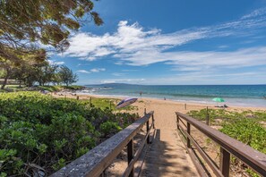 A wooden boardwalk leading to a beach with a clear sky and ocean view.