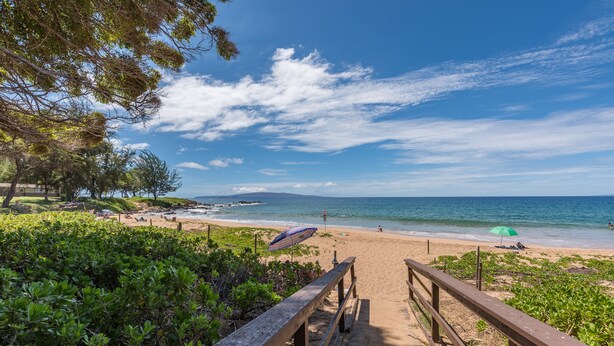 Ein hölzerner Steg führt zu einem Strand mit klarem Himmel und Meerblick.