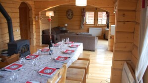 L’intérieur chaleureux d’un chalet en bois comprend un coin repas préparé pour un repas, un salon avec un canapé et une cheminée bien visible.