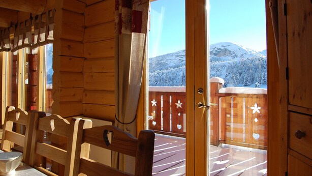 Une cabane en bois dotée d’un balcon, de meubles en bois et offrant une vue sur une montagne enneigée.