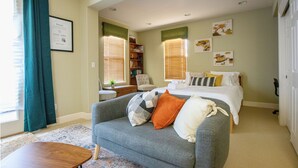 A cozy room with a grey sofa, a wooden coffee table, a bed with white bedding, and a bookshelf. - The Library (Dublin)