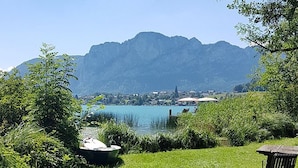 Vista al lago con montañas al fondo, un espacio con césped y una banca.